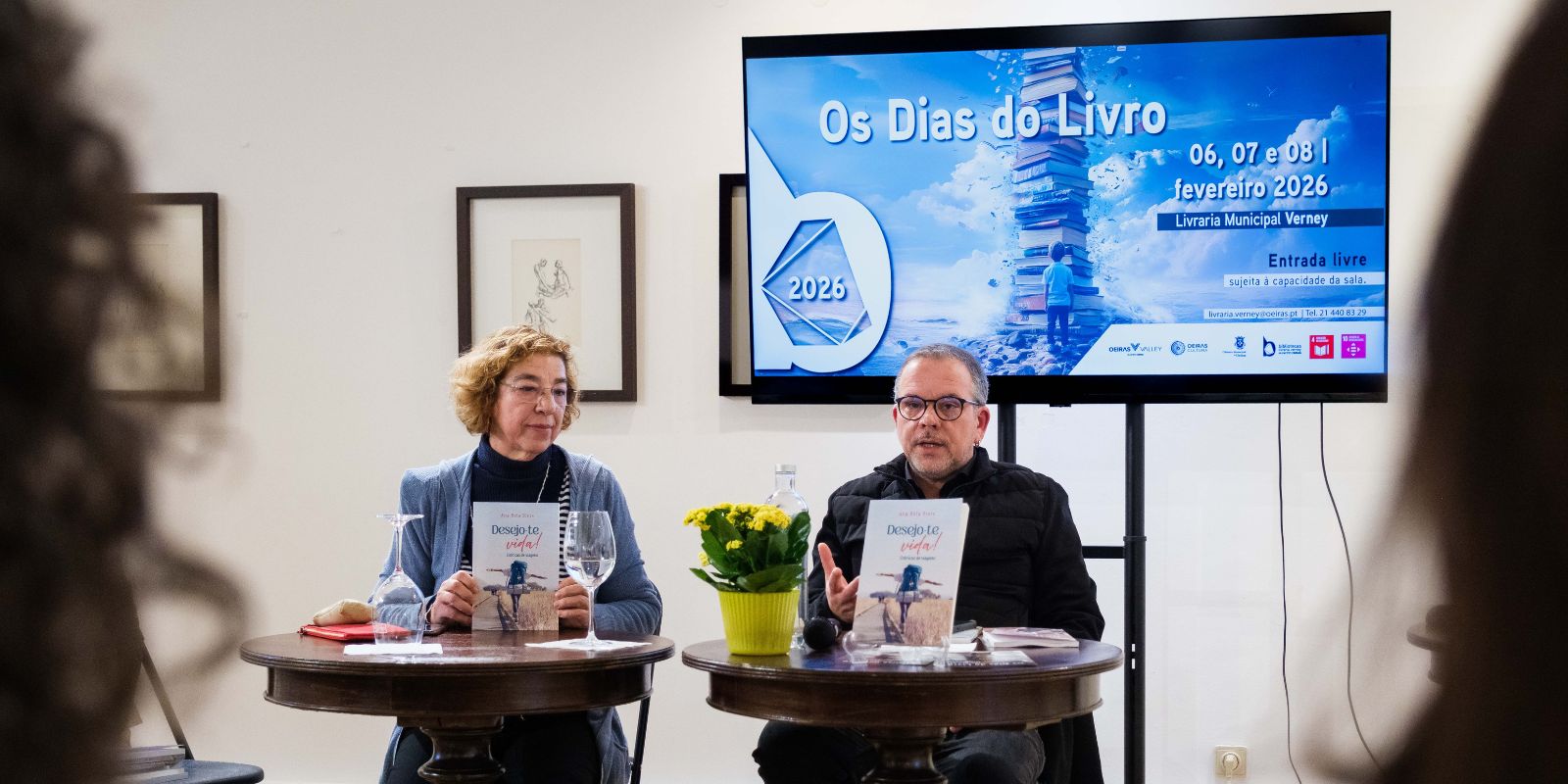 foto dos autores sentados com uma apresentação da imagem do evento atrás