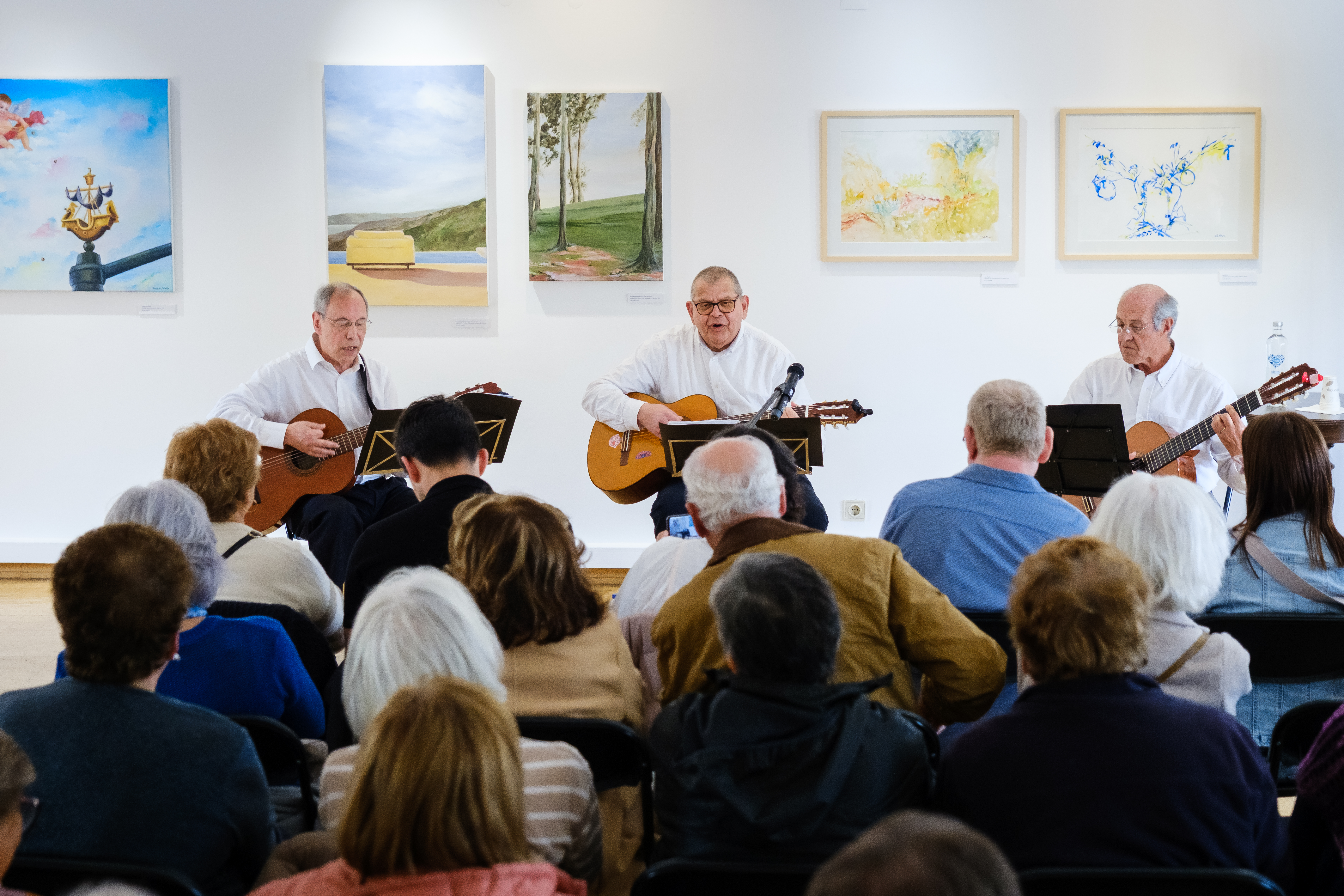 três músicos a tocar guitarra e a cantar perante sala cheia