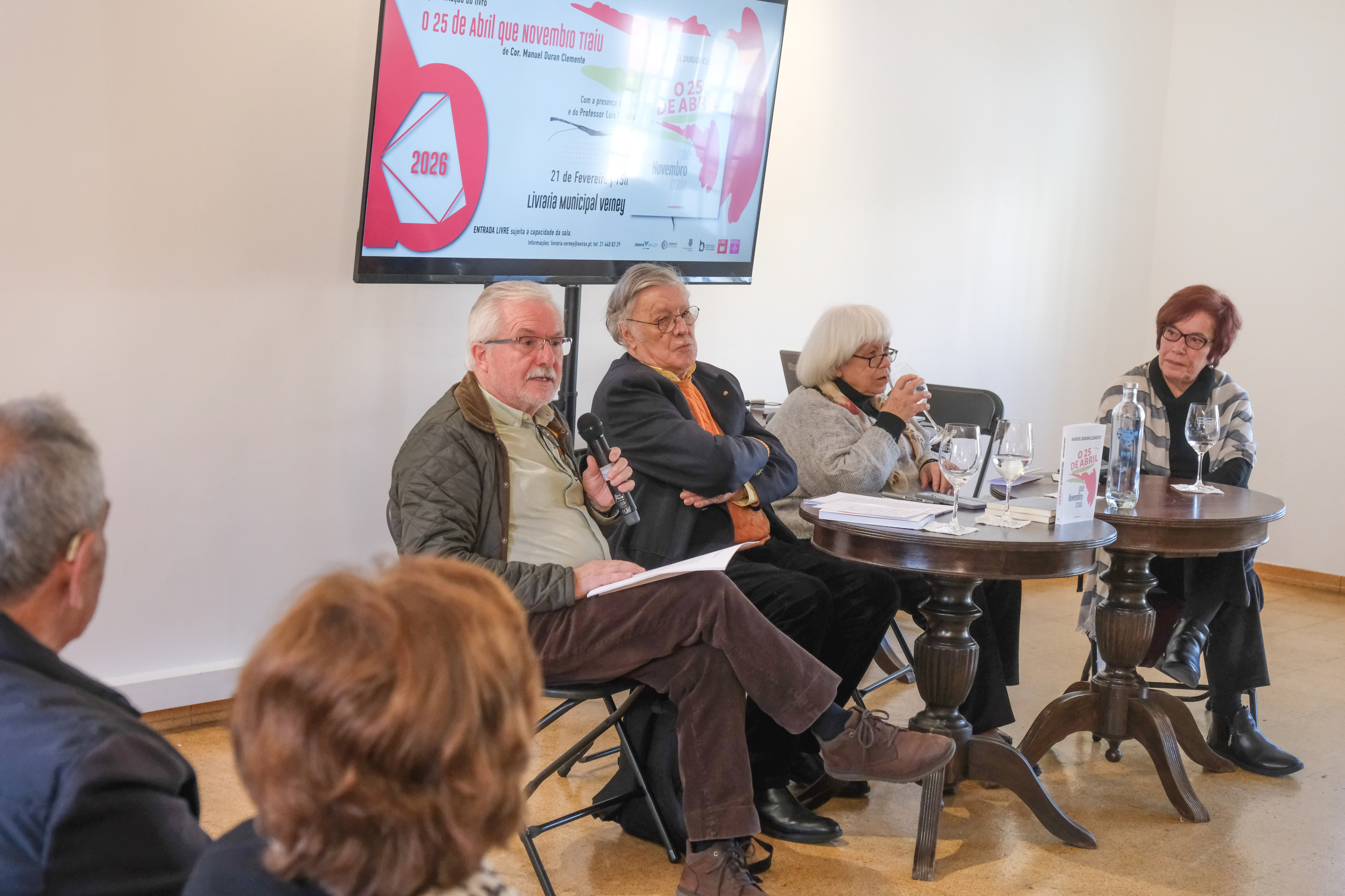 Painel integrado por dois senhores e duas senhoras sentados com uma televisão com o banner com o nome do evento