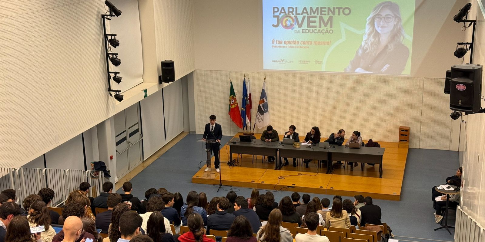 Jovem a discursar perante auditório lotado de jovens 